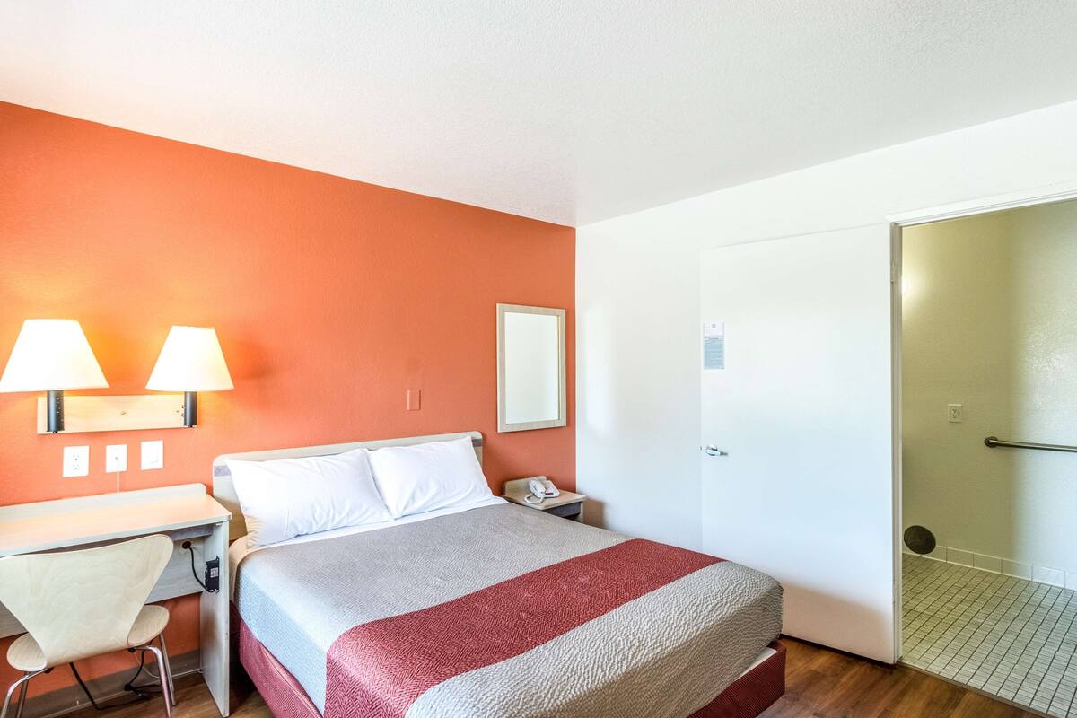 A hotel room with a bed, desk, chair, and a door leading to a bathroom.