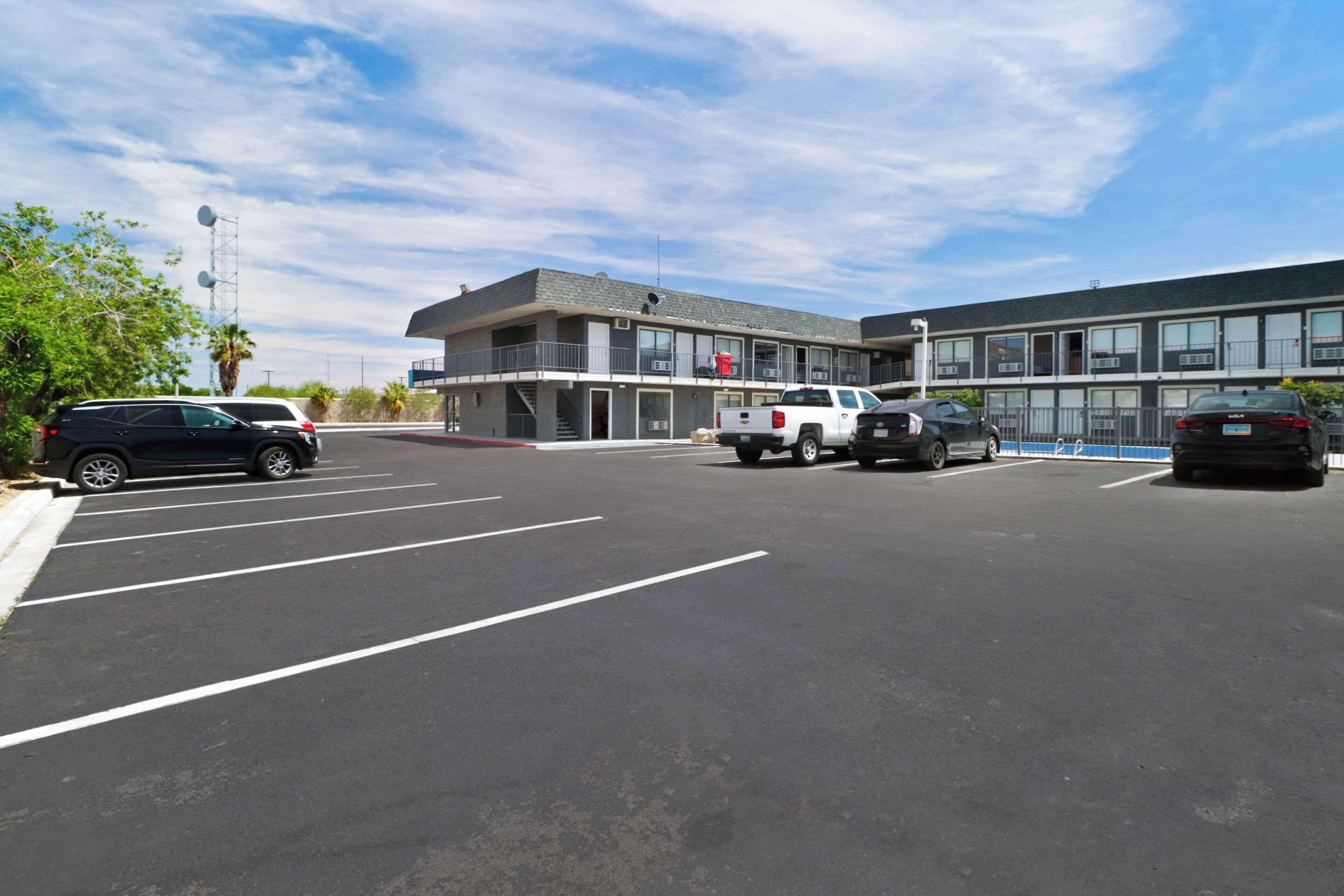 A parking lot with several vehicles, a building with a flat roof and large windows, and a clear sky.