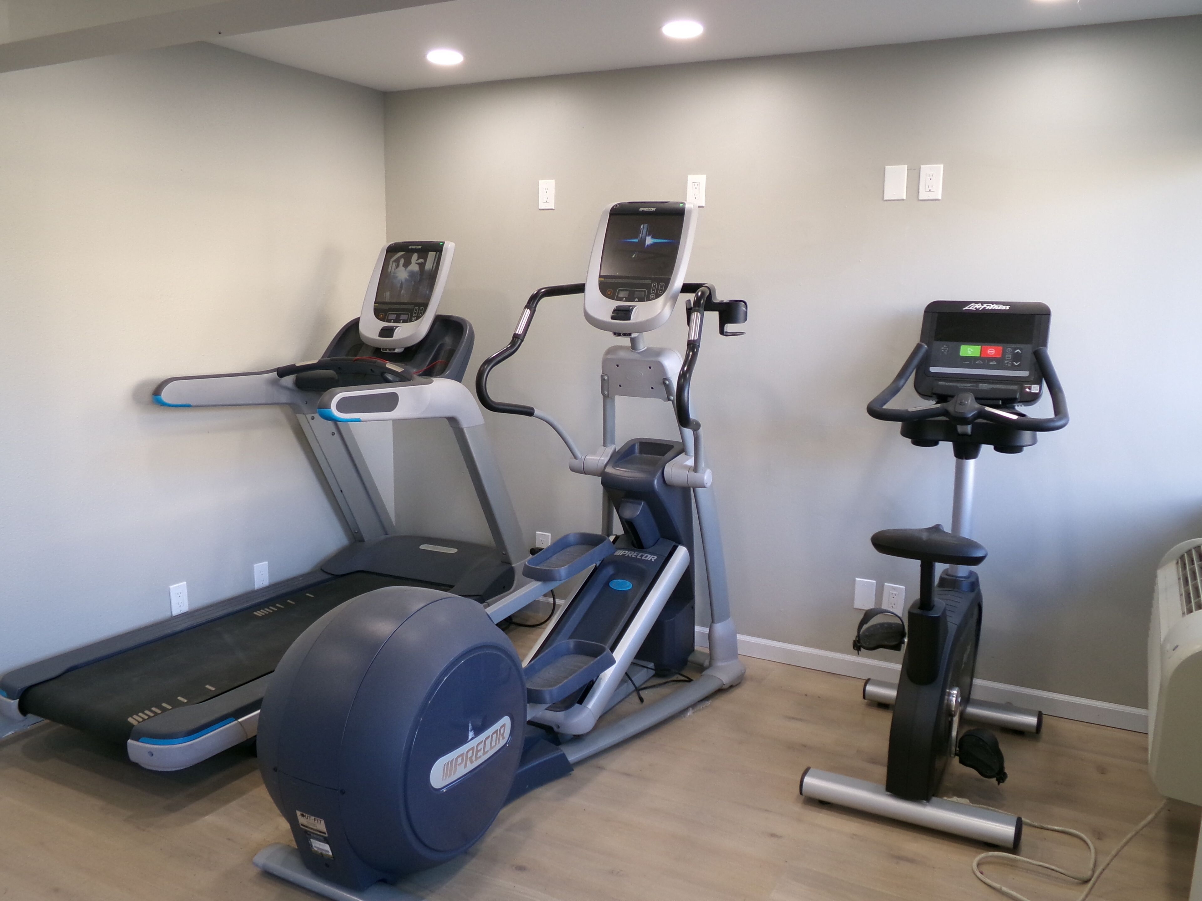 A home gym with three exercise machines: a treadmill, an elliptical, and a stationary bike.
