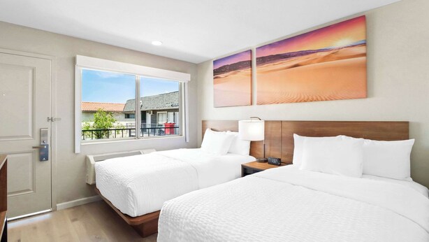 A hotel room with two beds, a window with a view of buildings, and a painting of a desert landscape. - Clarion Pointe Ridgecrest near China Lake Naval Station (Ridgecrest)