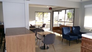A modern interior with wooden tables and chairs, a leather sofa, and large windows offering views of the outdoors. - Clarion Pointe Ridgecrest near China Lake Naval Station (Ridgecrest)