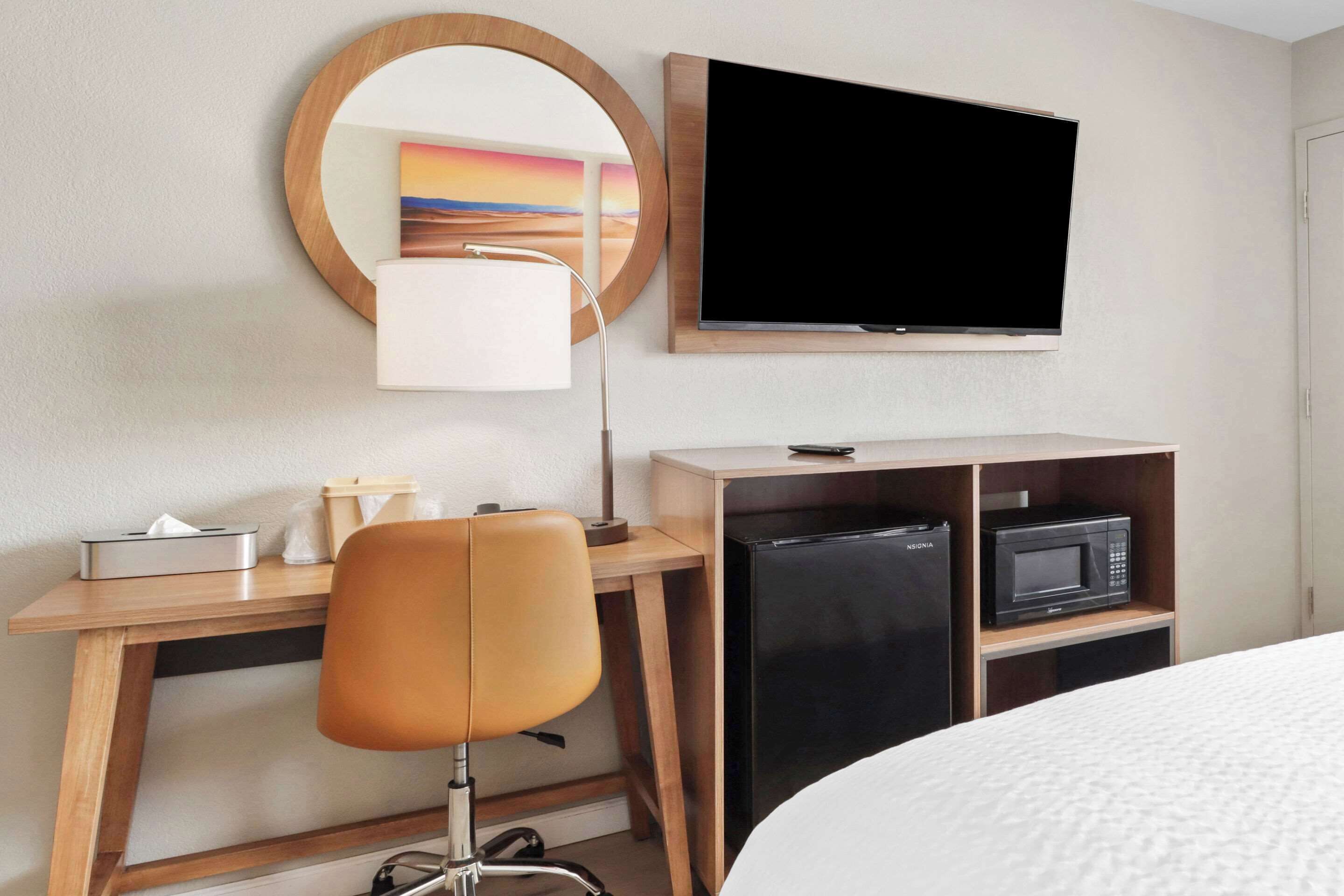 A hotel room with a bed, a desk with a chair, a TV, a microwave, and a refrigerator.