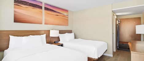 A hotel room with two beds, a wooden headboard, a nightstand with a lamp, and a large painting of a desert landscape.