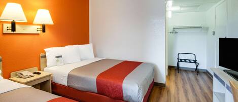 A hotel room with two beds, a TV, a desk with a lamp, and a walk-in closet.
