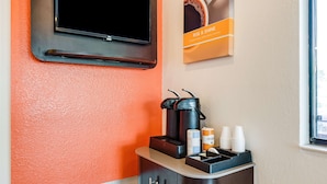 A coffee station with a coffee maker, cups, and a sign that reads "RISE & SHINE".