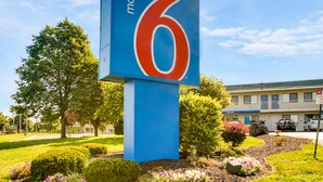 A motel sign with the number 6, surrounded by landscaped gardens and a building in the background.