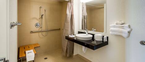 A bathroom with a shower, a sink, a mirror, and a towel rack.