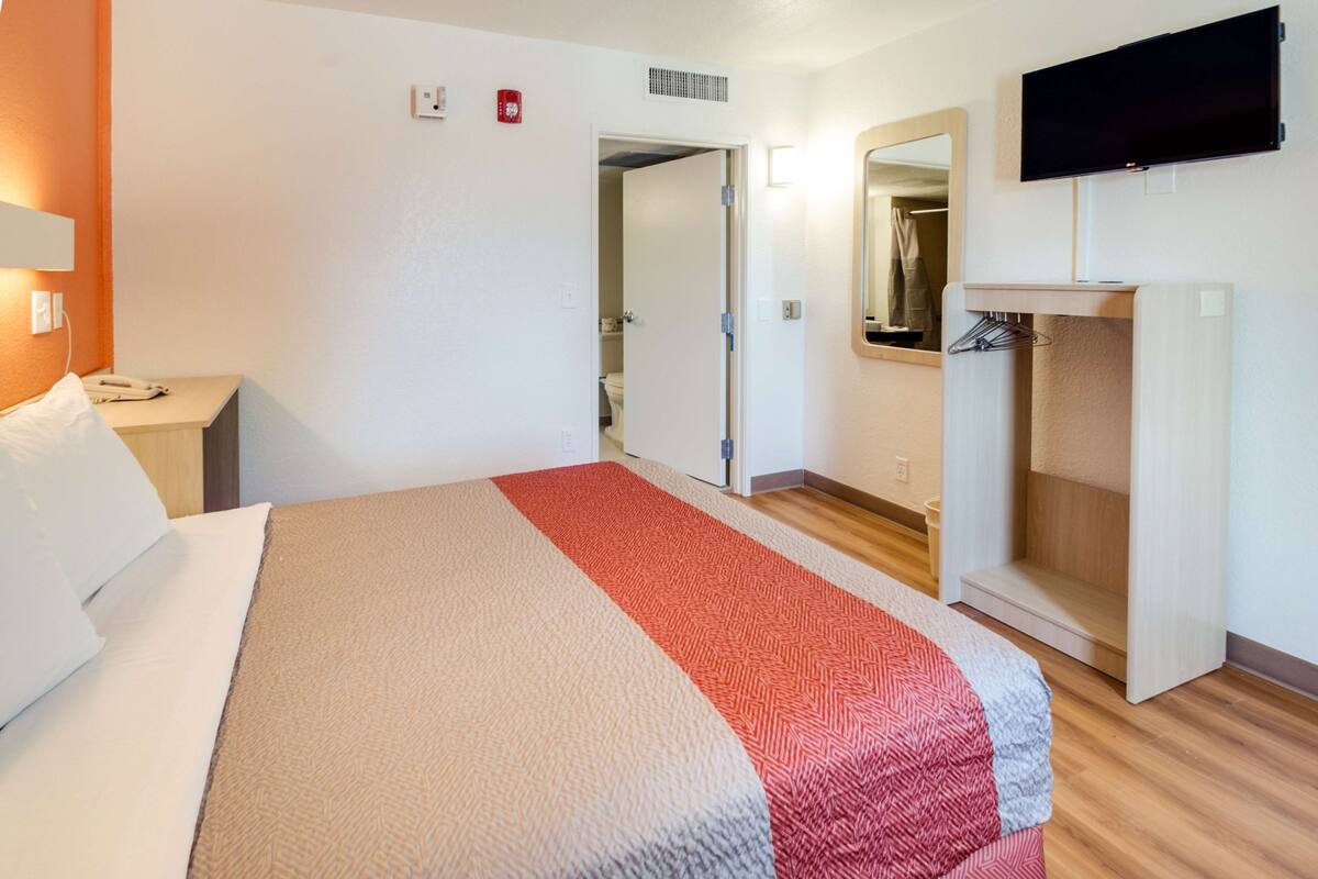 A hotel room with a bed, a bedside table with a phone, a TV mounted on the wall, a mirror, and a wardrobe.