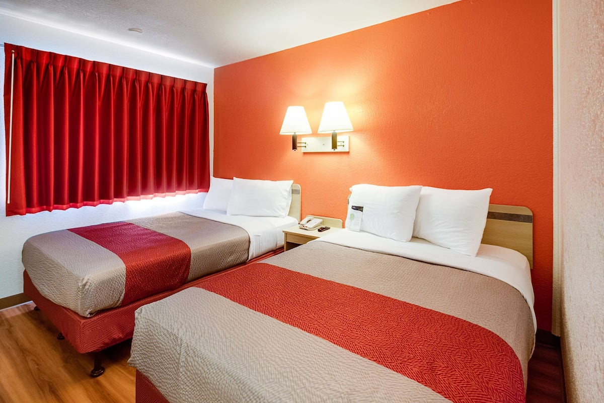A hotel room with two beds, red curtains, and wall-mounted lamps.
