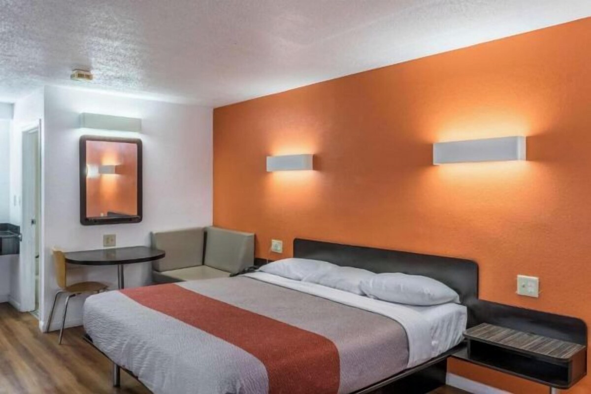 Ett hotellrum med en säng, sängbord, en stol och ett litet bord.
