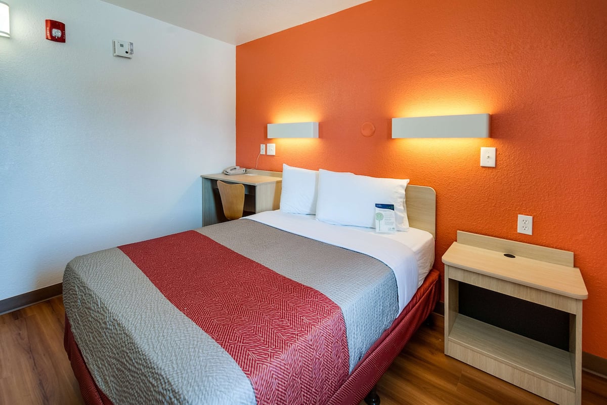 A hotel room with a bed, bedside tables, a desk, and a chair.