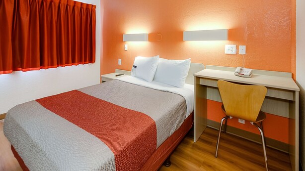 A hotel room with a bed, a desk, a chair, and a window with curtains.