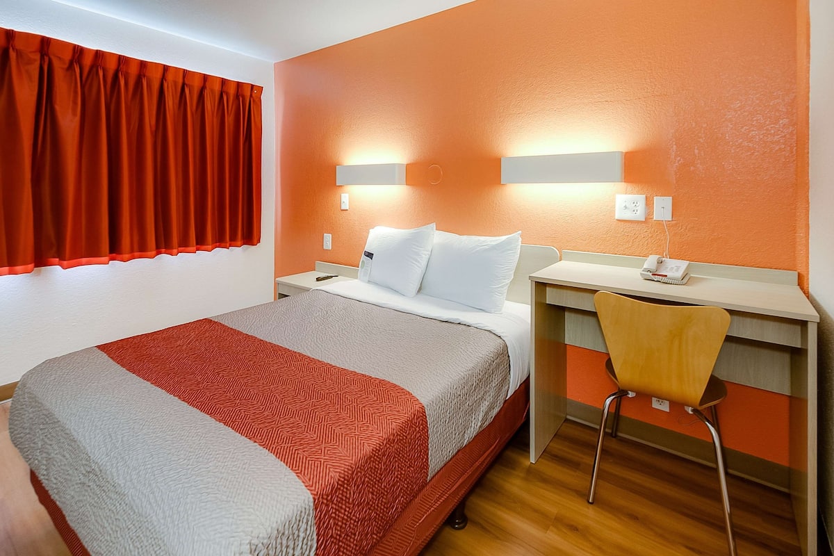 A hotel room with a bed, a desk, a chair, and a window with curtains.