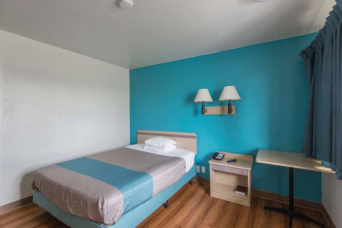 A hotel room with a bed, a desk, a phone, and a lamp.