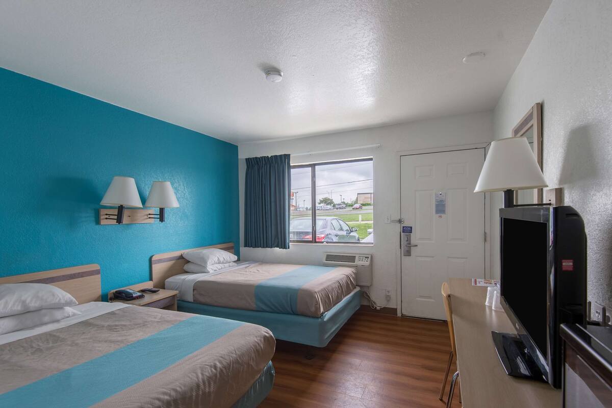 A hotel room with two beds, a TV, a desk, and a window with curtains.