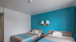 A hotel room with two single beds, a nightstand with a phone, and two wall-mounted lamps. - Motel 6 Kansas City, MO - Airport (Kansas City)