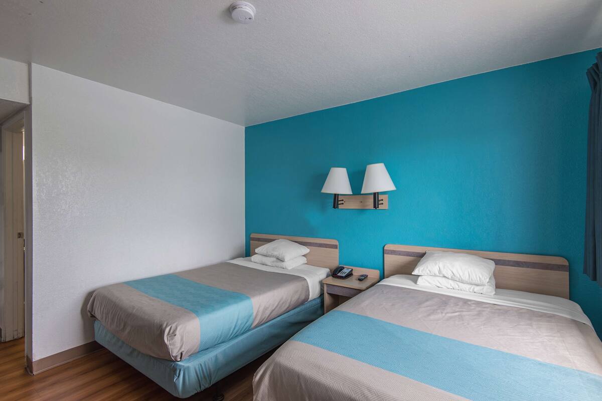 A hotel room with two single beds, a nightstand with a phone, and two wall-mounted lamps.