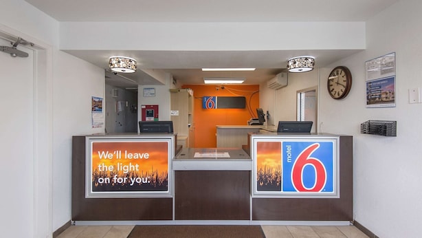 A hotel reception area with a desk, a clock, and a sign indicating room number 6. - Motel 6 Kansas City, MO - Airport (Kansas City)