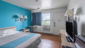 A hotel room with a bed, a desk with a TV, a window with curtains, and a door. - Motel 6 Kansas City, MO - Airport (Kansas City)