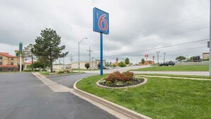 A motel sign with the number 6, a parking lot, and a grassy area with a flower bed. - Motel 6 Kansas City, MO - Airport (Kansas City)