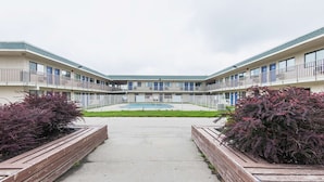 A motel with a central courtyard, a swimming pool, and a fenced area with shrubs. - Motel 6 Kansas City, MO - Airport (Kansas City)
