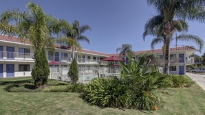 A hotel with multiple balconies, a swimming pool, and lush landscaping. - Motel 6 Corona, CA (Corona)