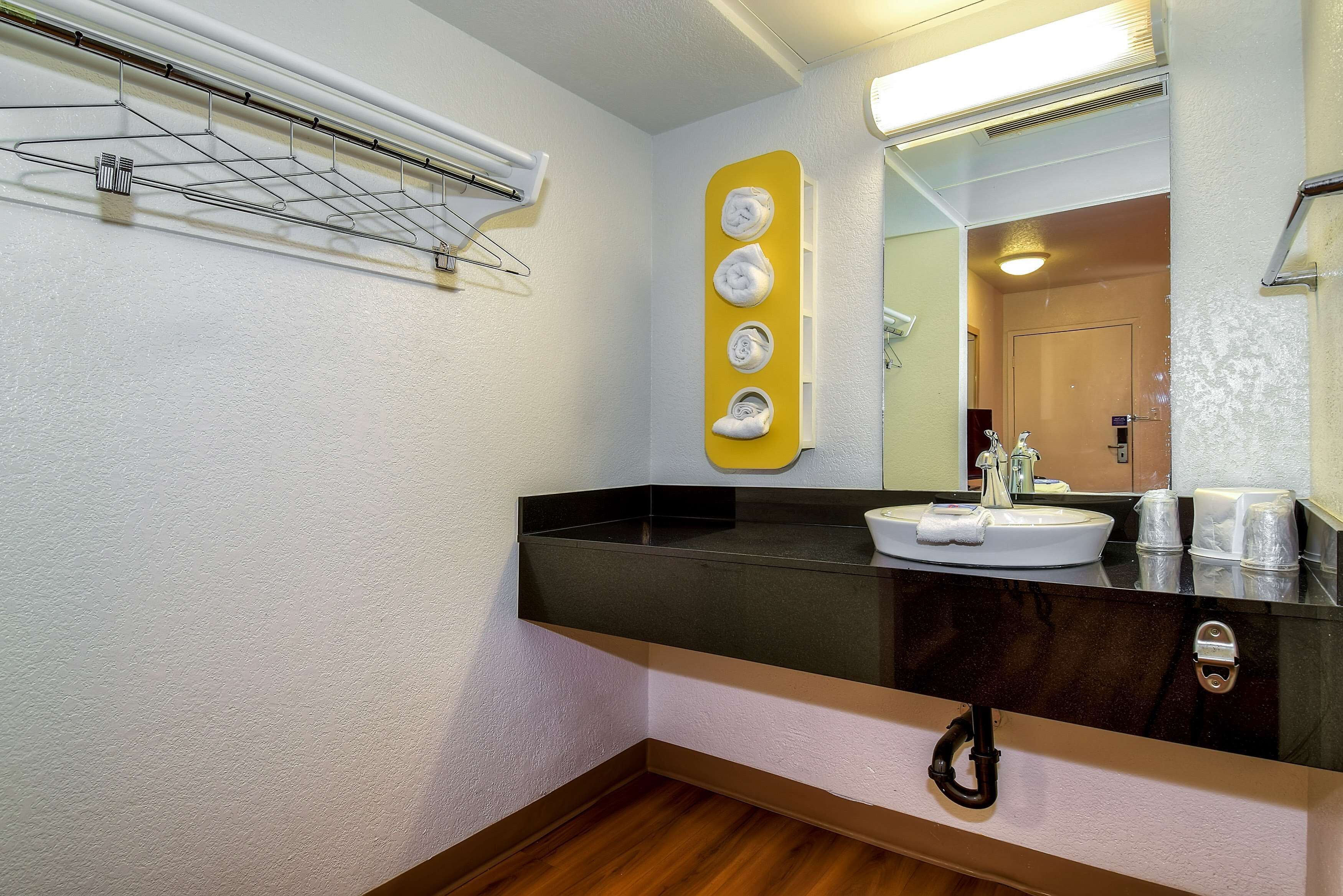 A bathroom with a black countertop, a white sink, a mirror, and a towel rack with towels.