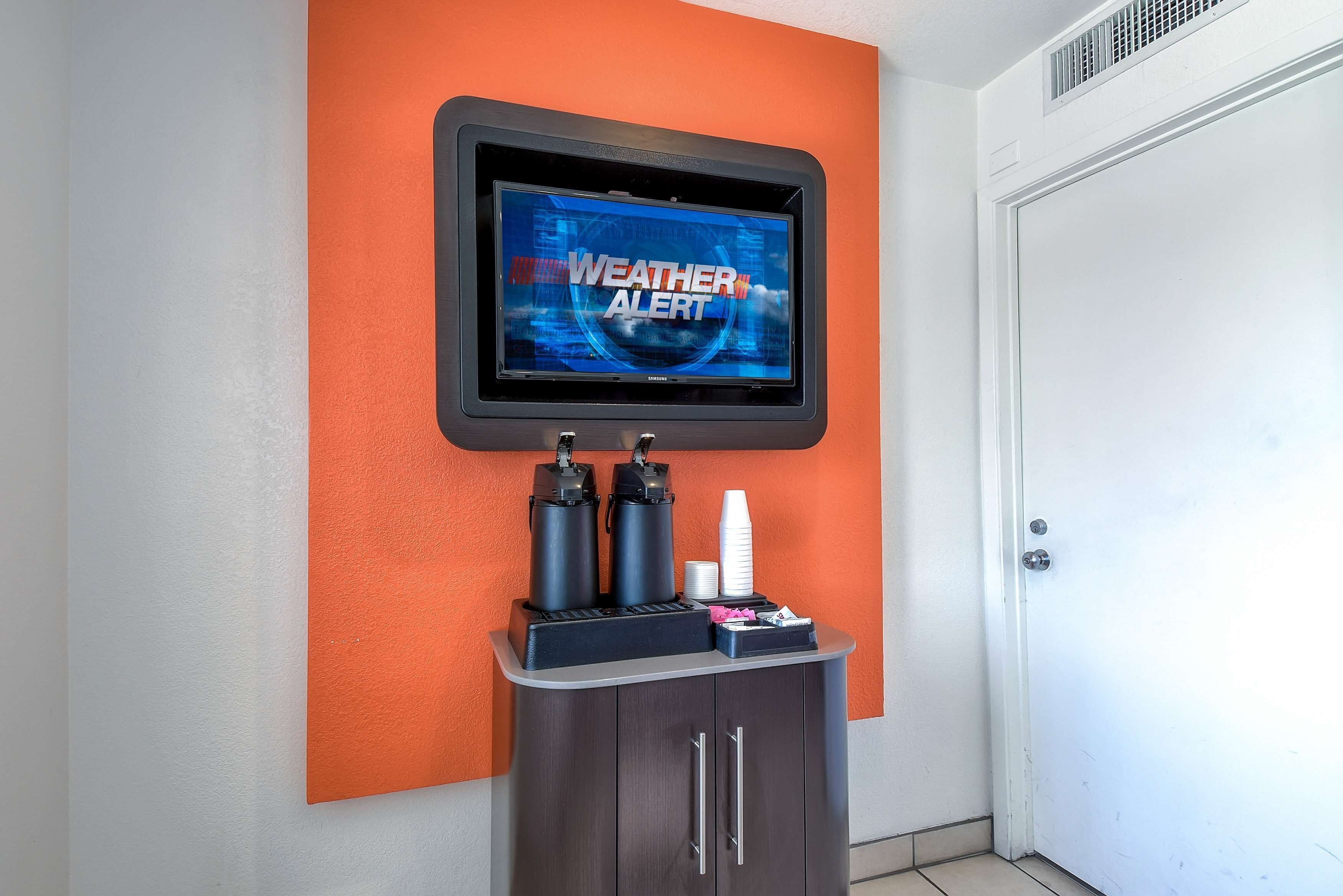 A weather alert display mounted on a wall, a coffee machine, and a cabinet with a door.