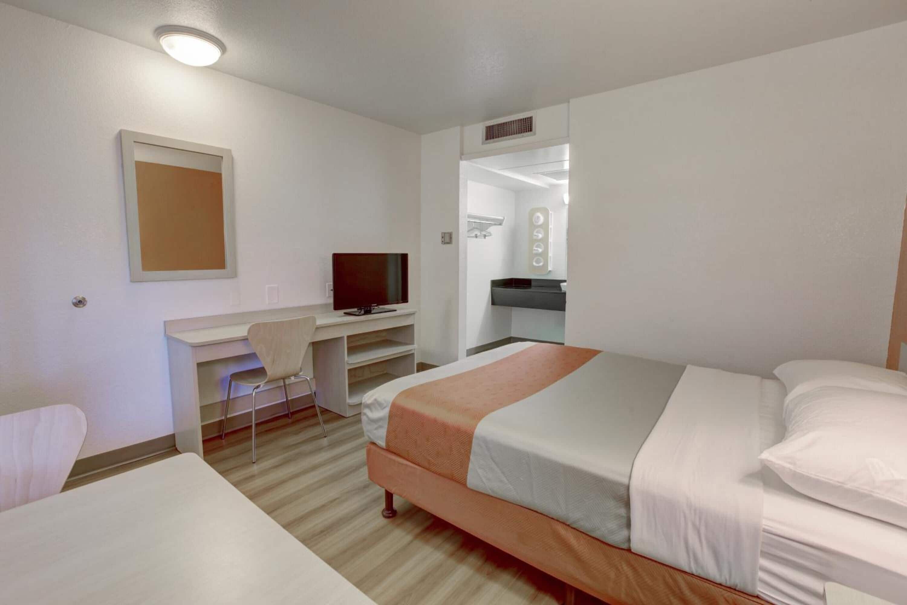 A hotel room with a bed, a desk with a chair, a television, and a mirror.