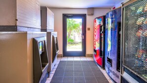 A hallway with vending machines, a door leading outside, and a Coca-Cola refrigerator. - Motel 6 Corona, CA (Corona)