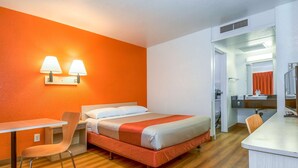 A hotel room with a bed, a desk, a chair, and a bathroom visible through an open door. - Motel 6 Corona, CA (Corona)