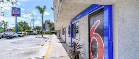 Entrada de un hotel con un cartel grande con el número '6', un letrero de bienvenida y un logotipo del número '6' en el edificio.