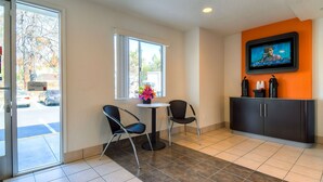 A hotel lobby with a reception desk, two chairs, a TV mounted on the wall, and a window with a view of the outside. - Motel 6 Rowland Heights, CA - Los Angeles - Pomona (Rowland Heights)