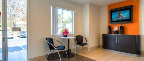 A hotel lobby with a reception desk, two chairs, a TV mounted on the wall, and a window with a view of the outside.