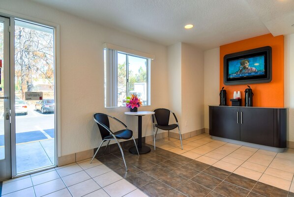A hotel lobby with a reception desk, two chairs, a TV mounted on the wall, and a window with a view of the outside. - Motel 6 Rowland Heights, CA - Los Angeles - Pomona (Rowland Heights)