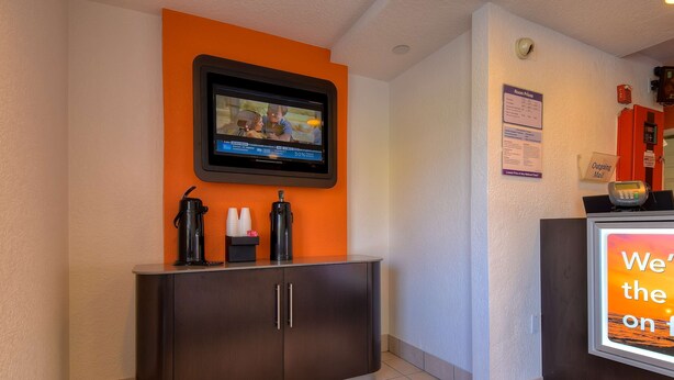 A reception area with a TV mounted on the wall, a coffee station, and a sign indicating room prices and an out-of-order mail slot. - Motel 6 Rowland Heights, CA - Los Angeles - Pomona (Rowland Heights)