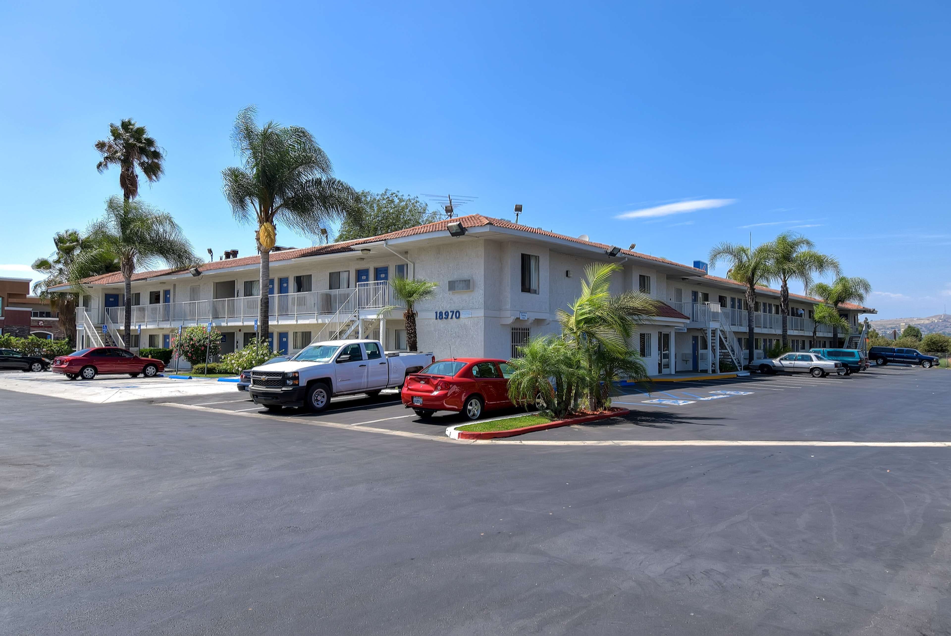 A multi-story motel with a red-tiled roof, several balconies, and a parking lot with various vehicles.