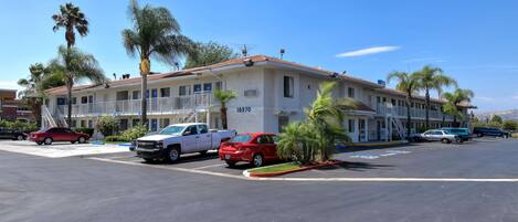 A multi-story motel with a red-tiled roof, several balconies, and a parking lot with various vehicles.