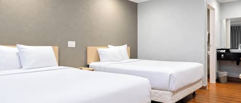 Habitación de hotel con dos camas, piso de madera, pared gris y baño con espejo y lavabo.