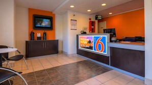 A hotel reception area with a digital screen, a counter with a phone, and a sign indicating the number 6. - Motel 6 Rowland Heights, CA - Los Angeles - Pomona (Rowland Heights)