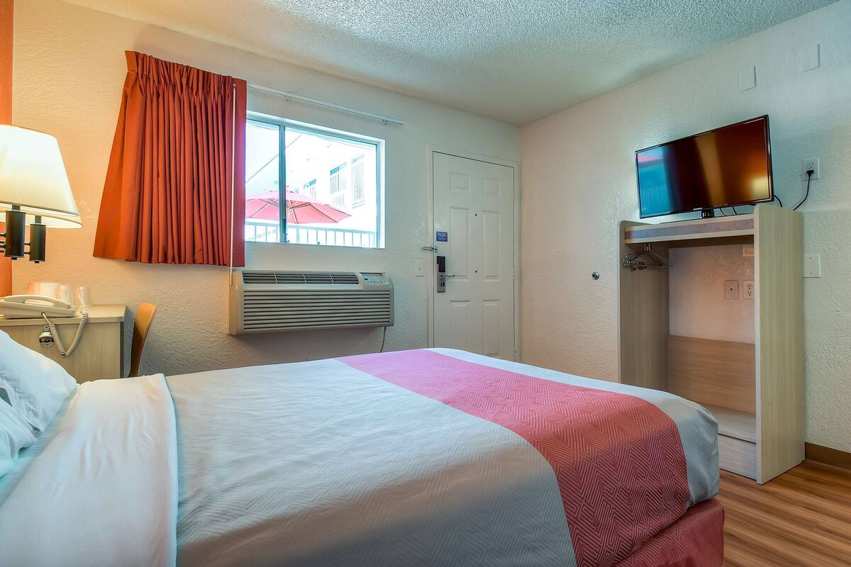 A hotel room with a bed, a TV, a wardrobe, a desk with a lamp, and a window with curtains.