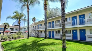 A motel with multiple blue doors, a covered parking area, and a well-maintained lawn with palm trees. - Motel 6 Rowland Heights, CA - Los Angeles - Pomona (Rowland Heights)
