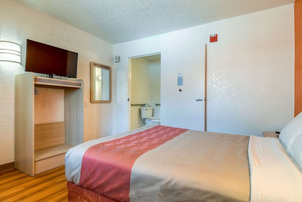 Habitación de hotel con cama, televisor montado en un estante de madera, armario y baño visible a través de una puerta abierta.