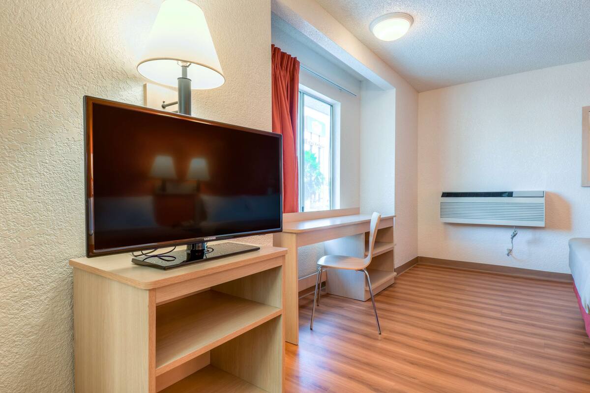 A modern room with a flat-screen TV, a desk, a chair, and a window with curtains.