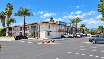 A motel with a 'Welcome' sign, multiple parking spaces, and palm trees.