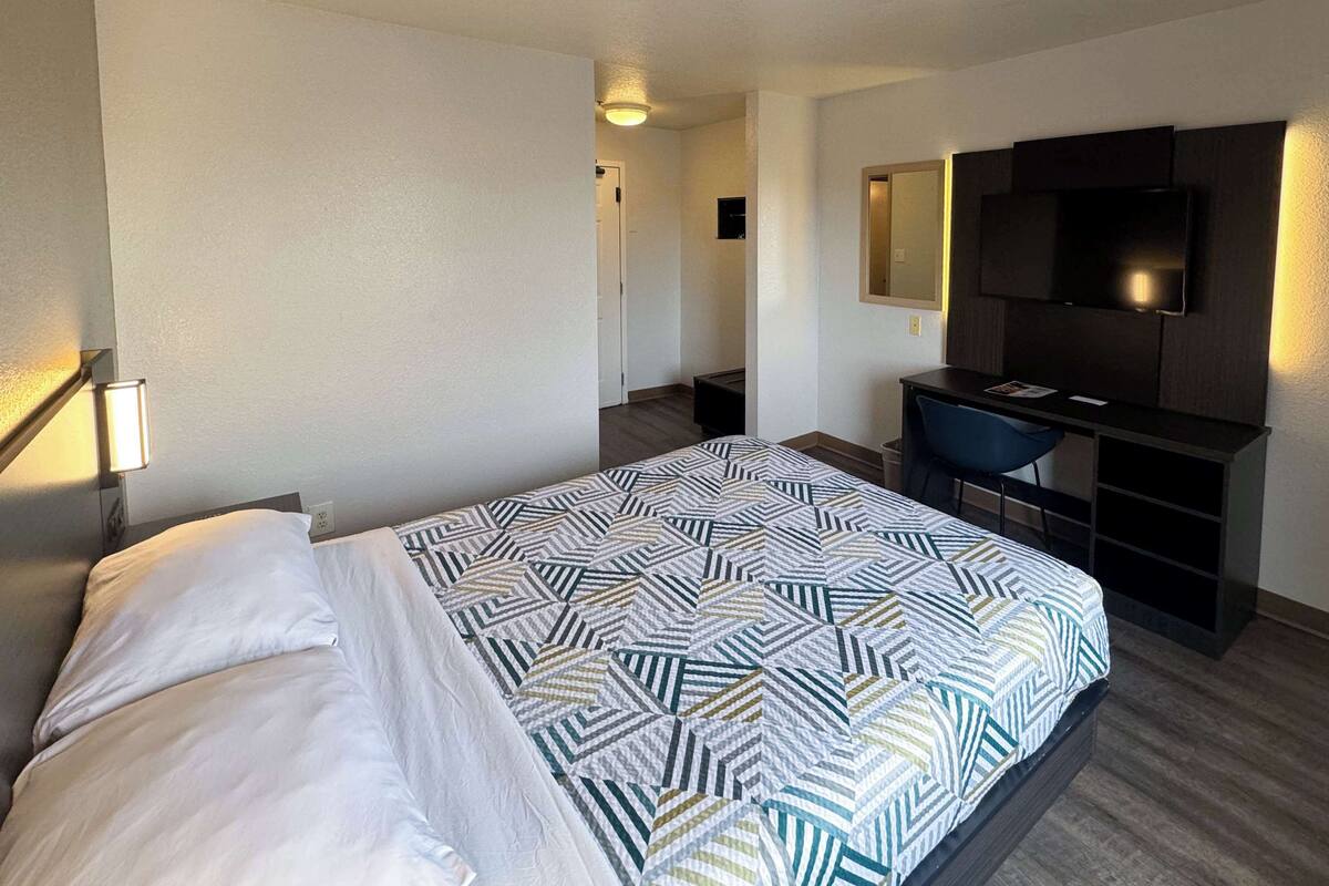 A hotel room with a bed, a desk, a chair, a TV, and a small window.