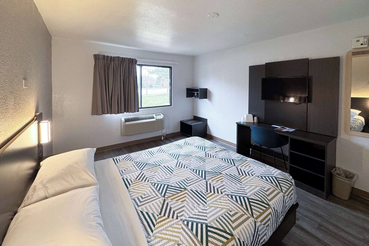 A hotel room with a bed, a desk, a TV, and a window with curtains.