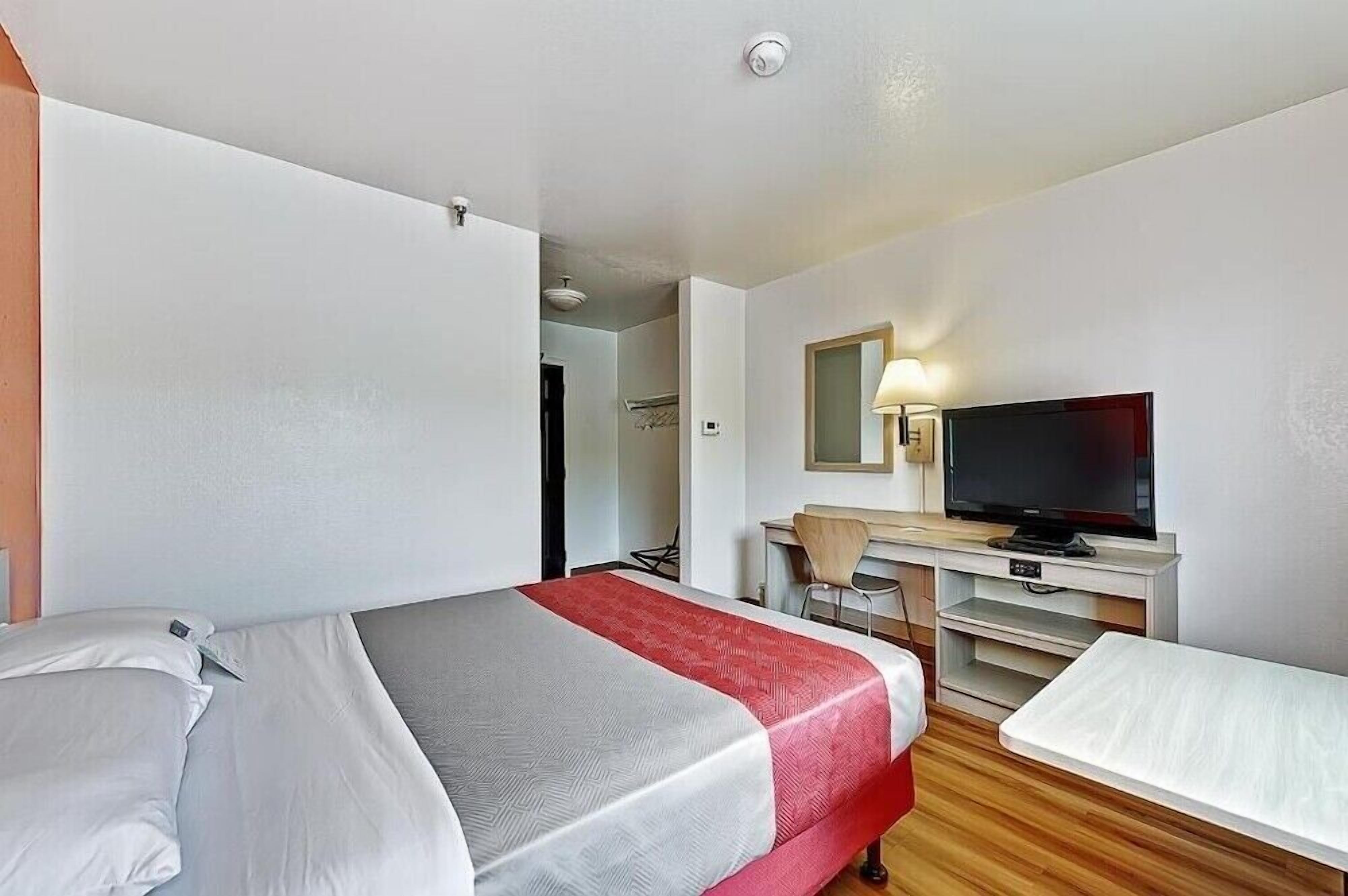 Ein Hotelzimmer mit Bett, Schreibtisch mit Stuhl, Fernseher und einem kleinen Tisch.