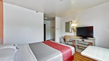A hotel room with a bed, a desk with a chair, a television, and a small table.