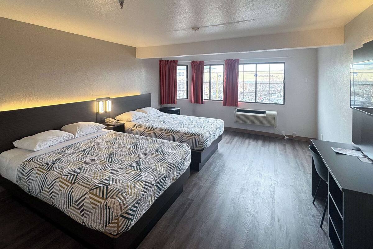 A hotel room with two beds, a desk, and a window with curtains.